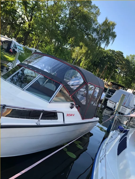 Kleines Motorboot mit rot eingefasstem transparentem Fahrverdeck in Seitenansicht.