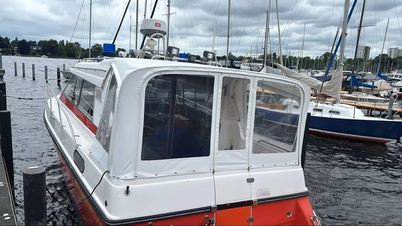 Rot-weißes Kajütboot am Hafen mit hellem geschlossenem Fahrverdeck.
