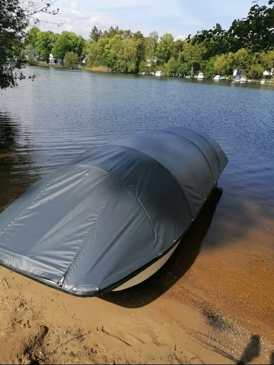 Abgestelltes Boot am Seeufer mit dunkelgrauer Ganzabdeckung.