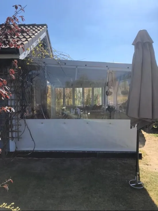 Terrasse mit transparentem PVC-Windschutz und Sonnenschirm im Außenbereich.
