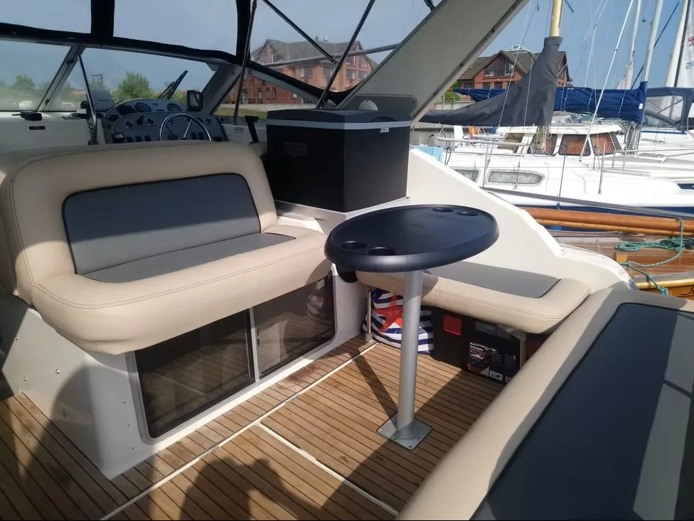 Cockpit eines Motorboots mit cremefarbener und dunkelblauer Sitzbank neben einem Tisch.