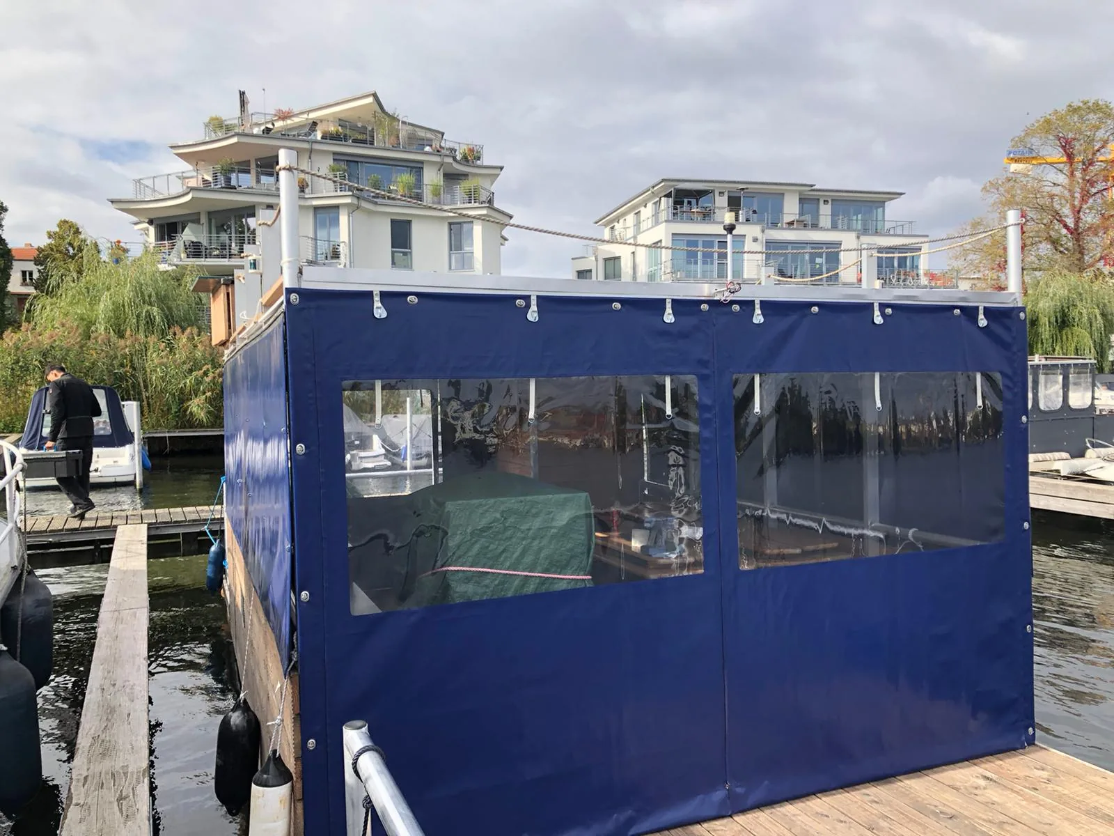 Dunkelblaue Einhausung mit transparenten Fenstern auf einer Plattform am Wasser.