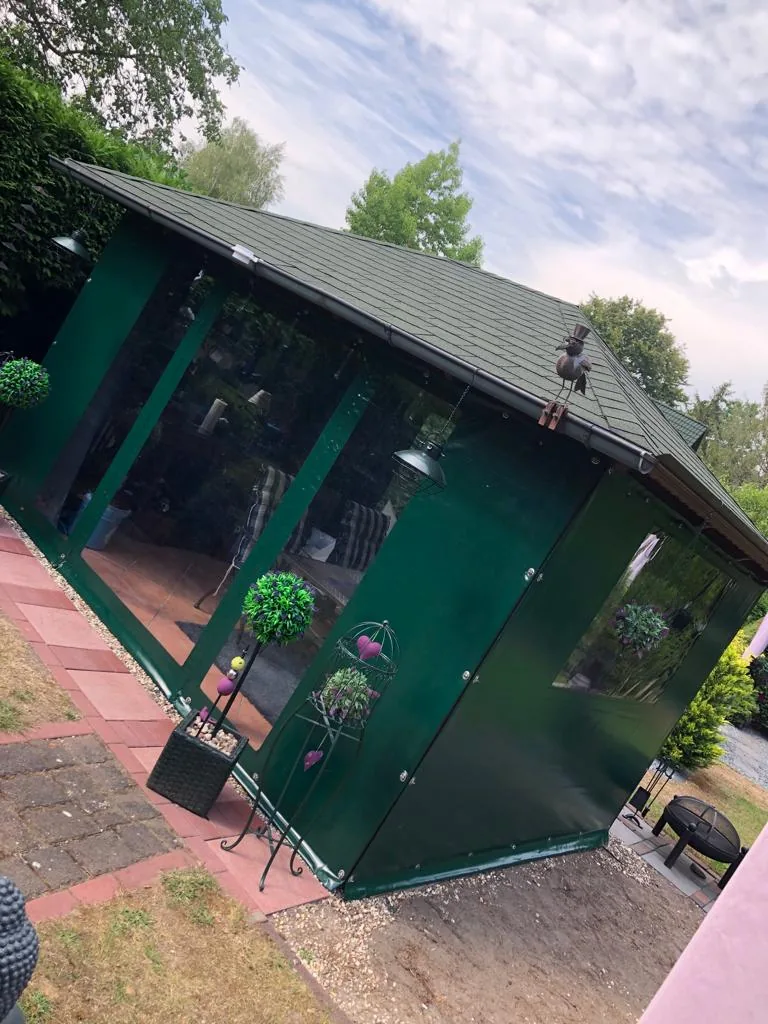 Grüne transparente Einhausung an einer überdachten Terrasse.