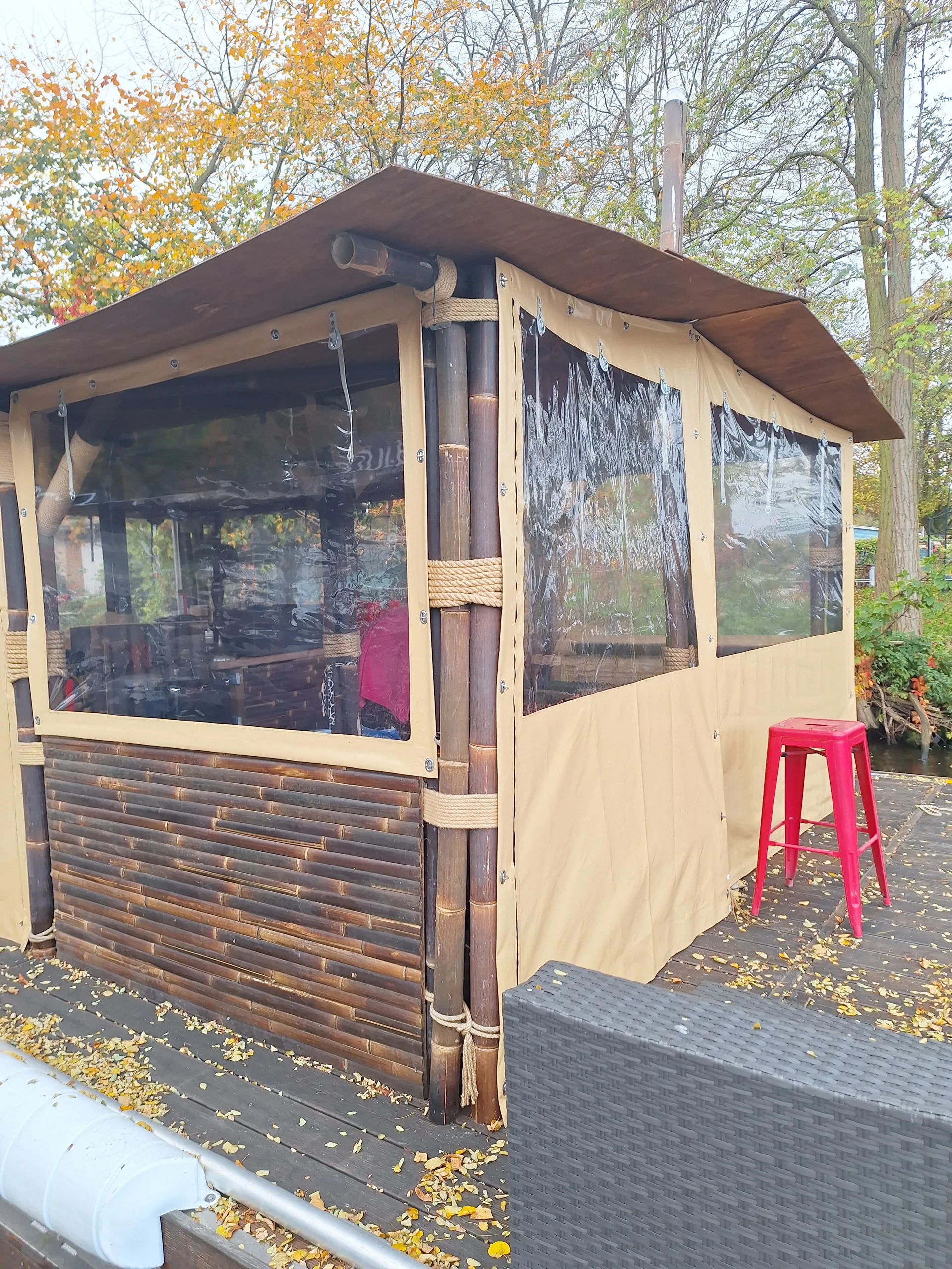 Beige Einhausung mit transparenten PVC-Fenstern an einem kleinen Holzpavillon.