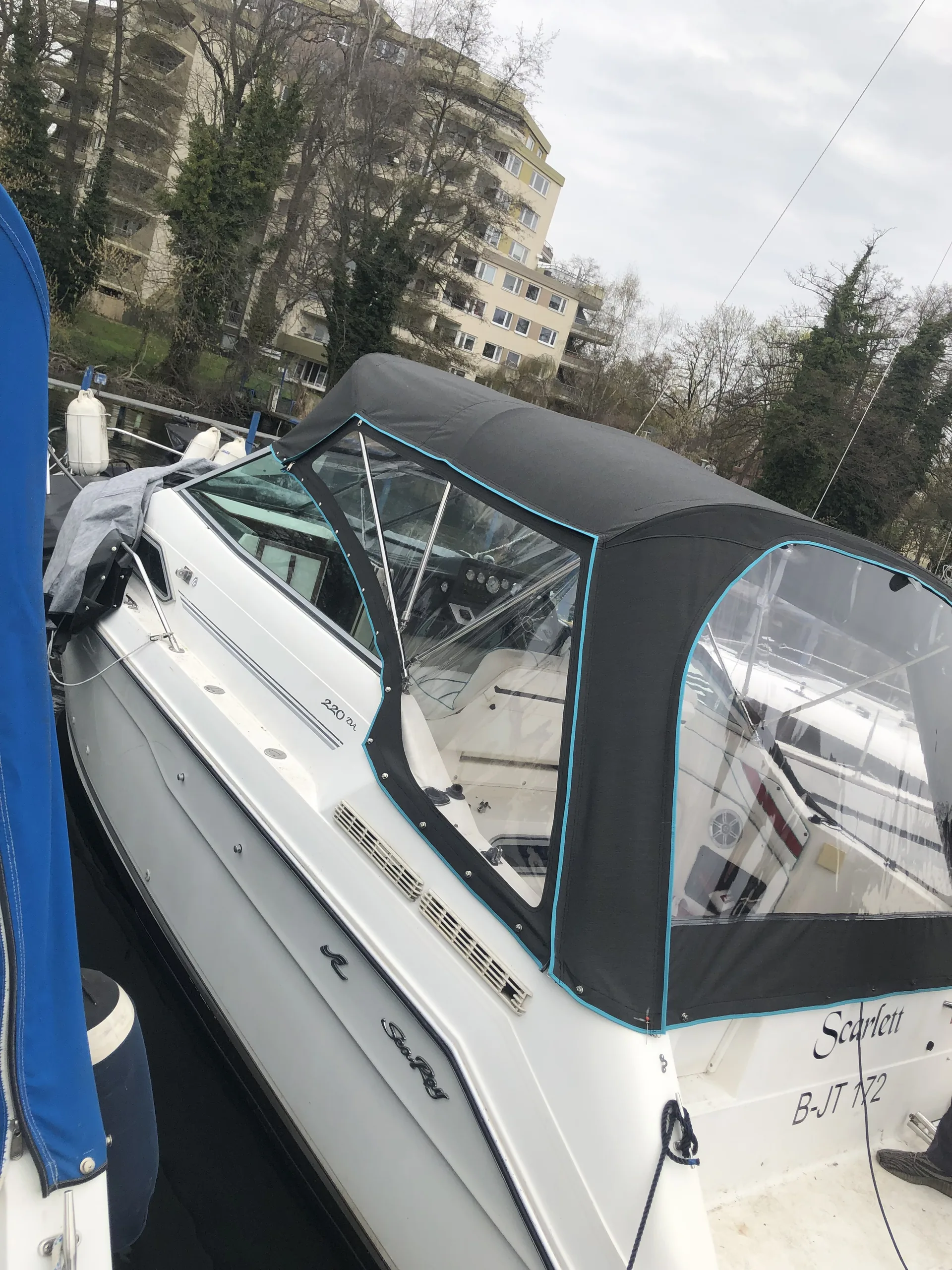 Passgenaue dunkle Fahrpersenning auf einem weißen Motorboot, seitlich am Scheibenrahmen fotografiert.