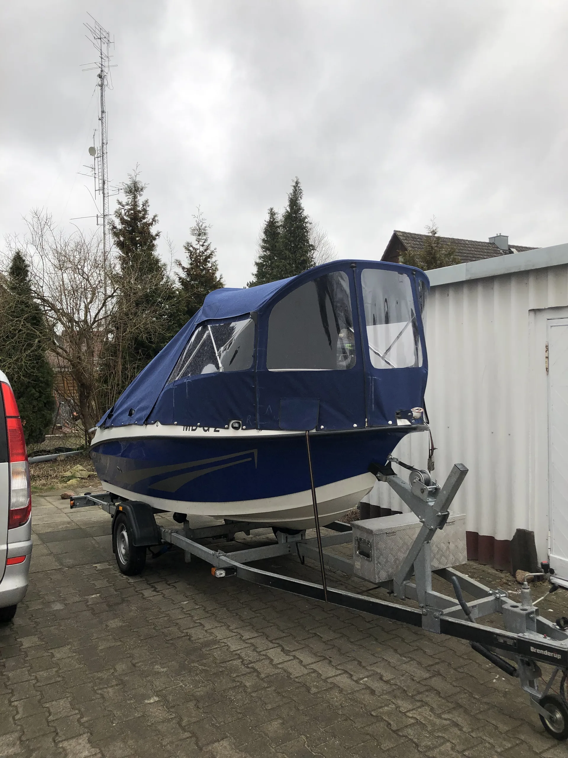 Blaues Motorboot mit dunkelblauer Fahrpersenning und klaren Seitenfenstern auf dem Trailer.