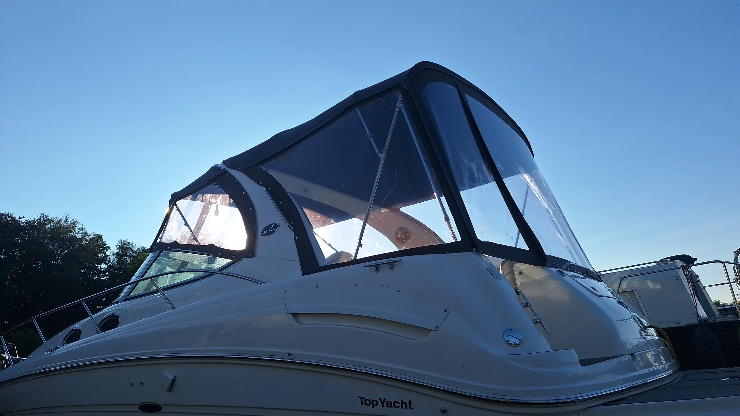 Blaue Motoryacht mit geschlossener dunkler Fahrpersenning und klaren Fenstern.