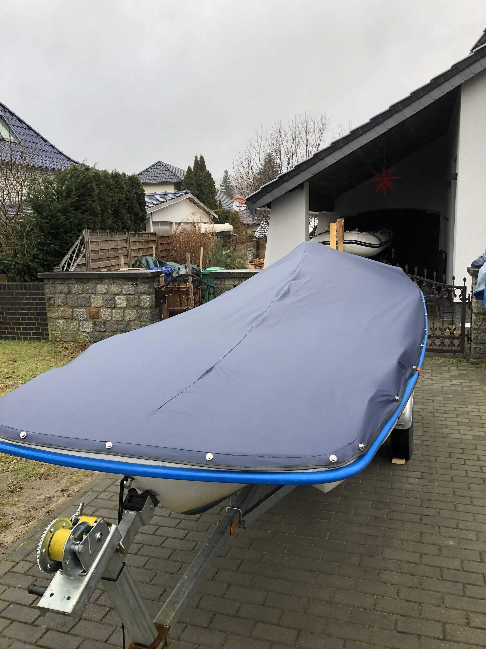 Blaues Boot auf einem Trailer mit dunkelgrauer Ganzabdeckung.