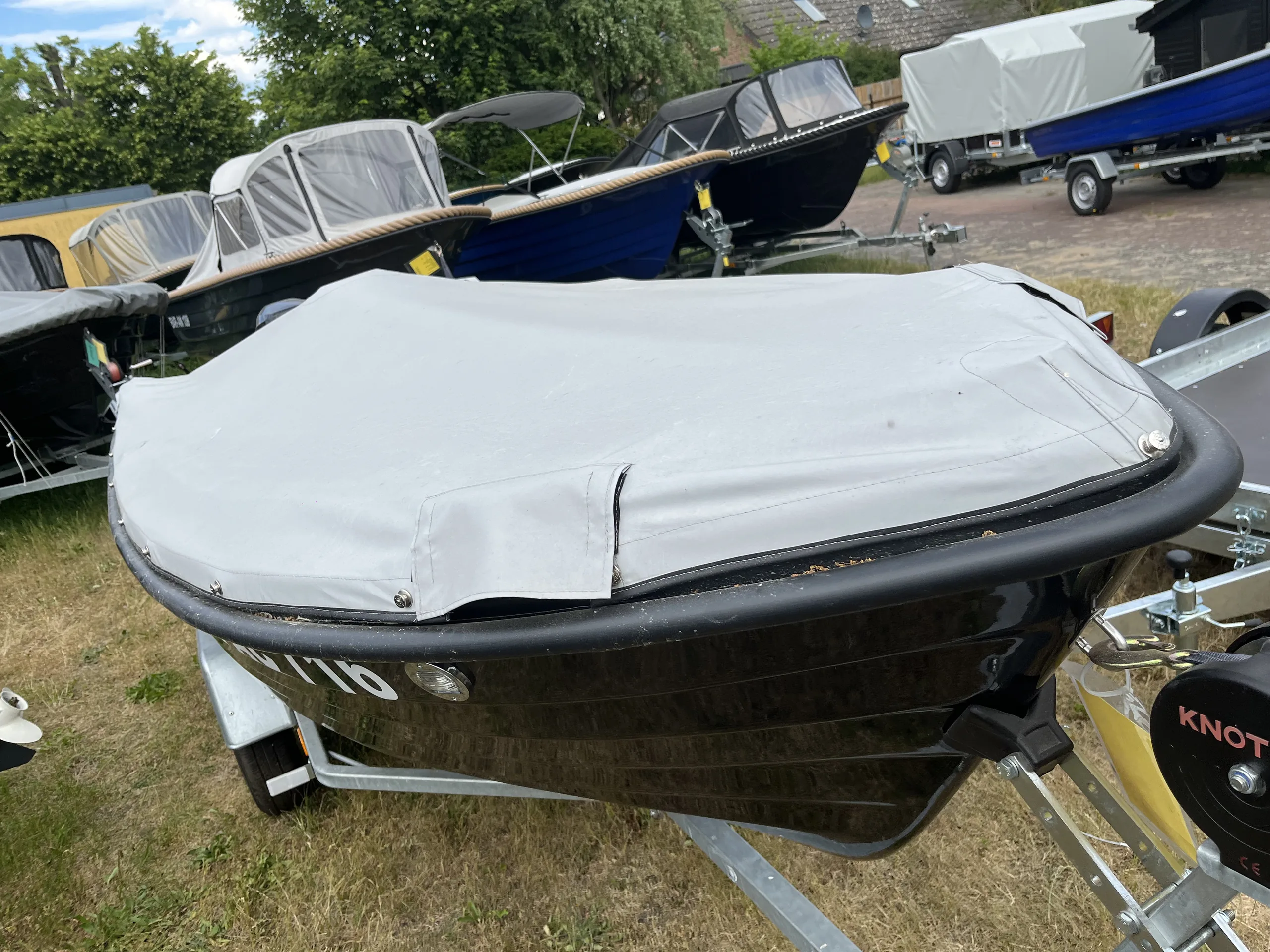 Schwarzes Motorboot mit heller passgenauer Abdeckung über dem offenen Innenraum.