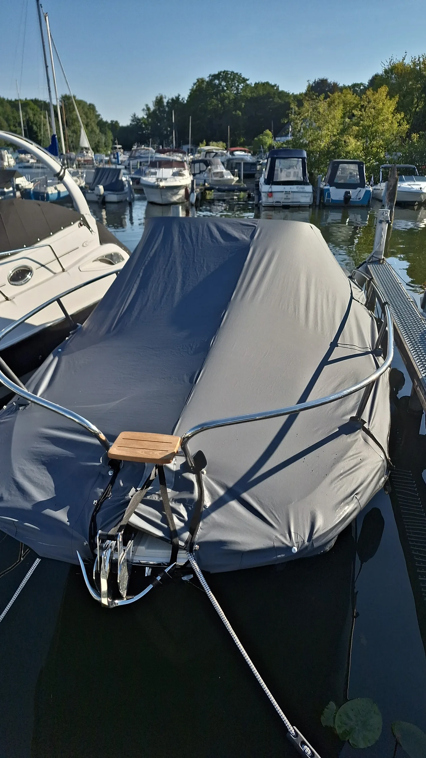 Motorboot mit dunkelblauer, hoch abgestützter Winterplane am Liegeplatz.