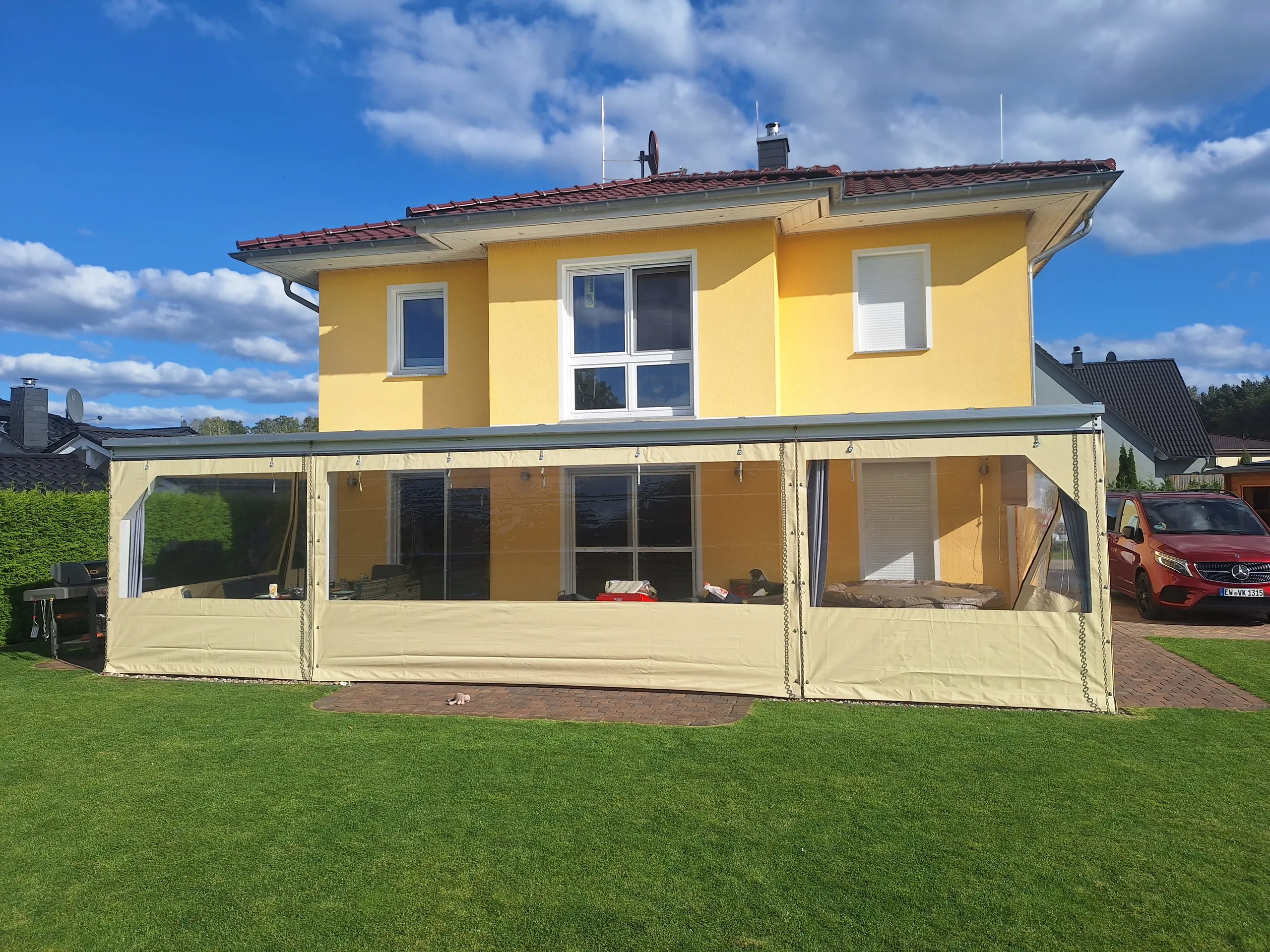 Beige PVC-Einhausung mit breiten transparenten Fensterfeldern an einer Terrasse.