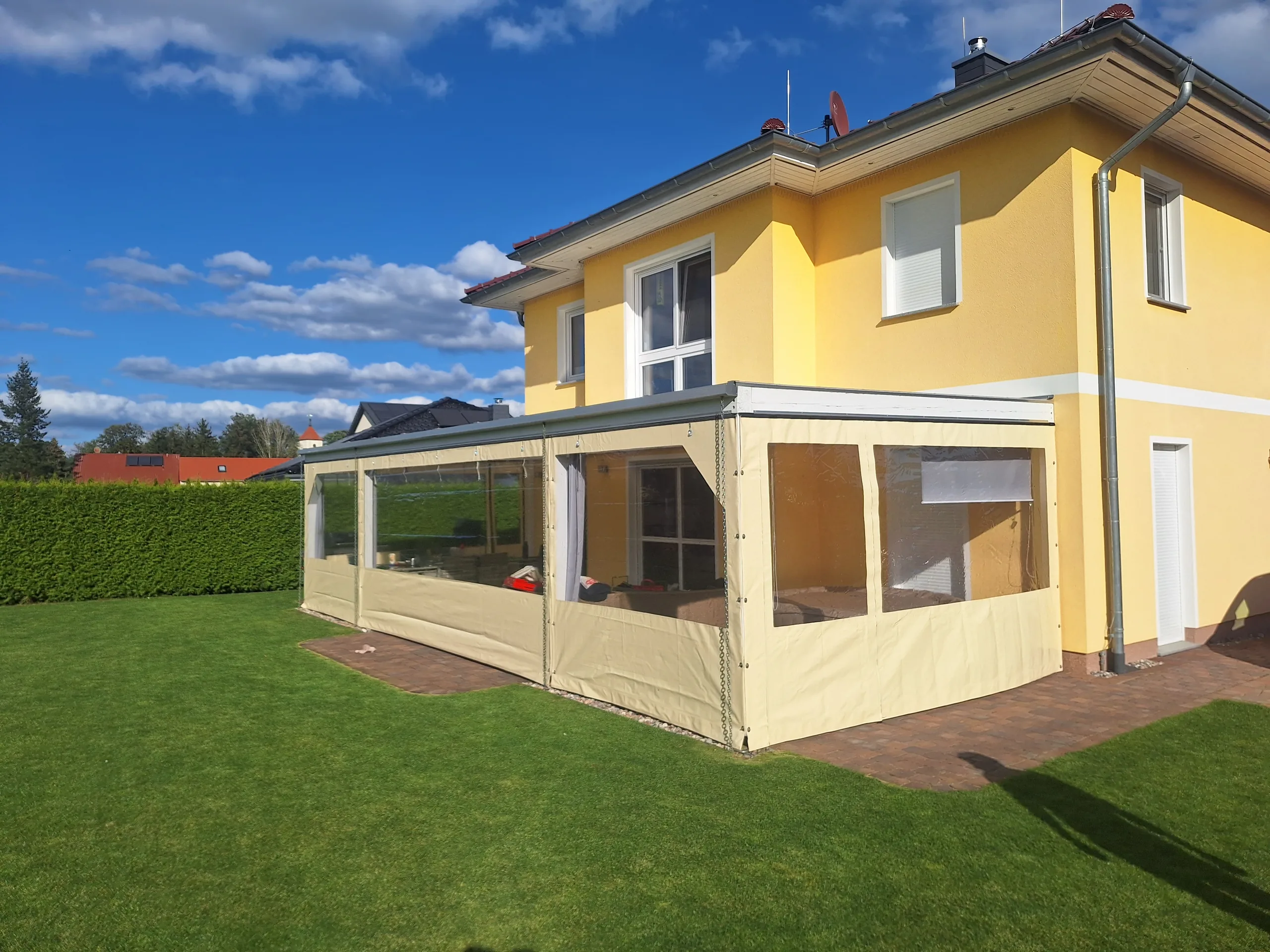 Seitliche Ansicht einer beigefarbenen Terrasseneinhausung mit transparenten Feldern.