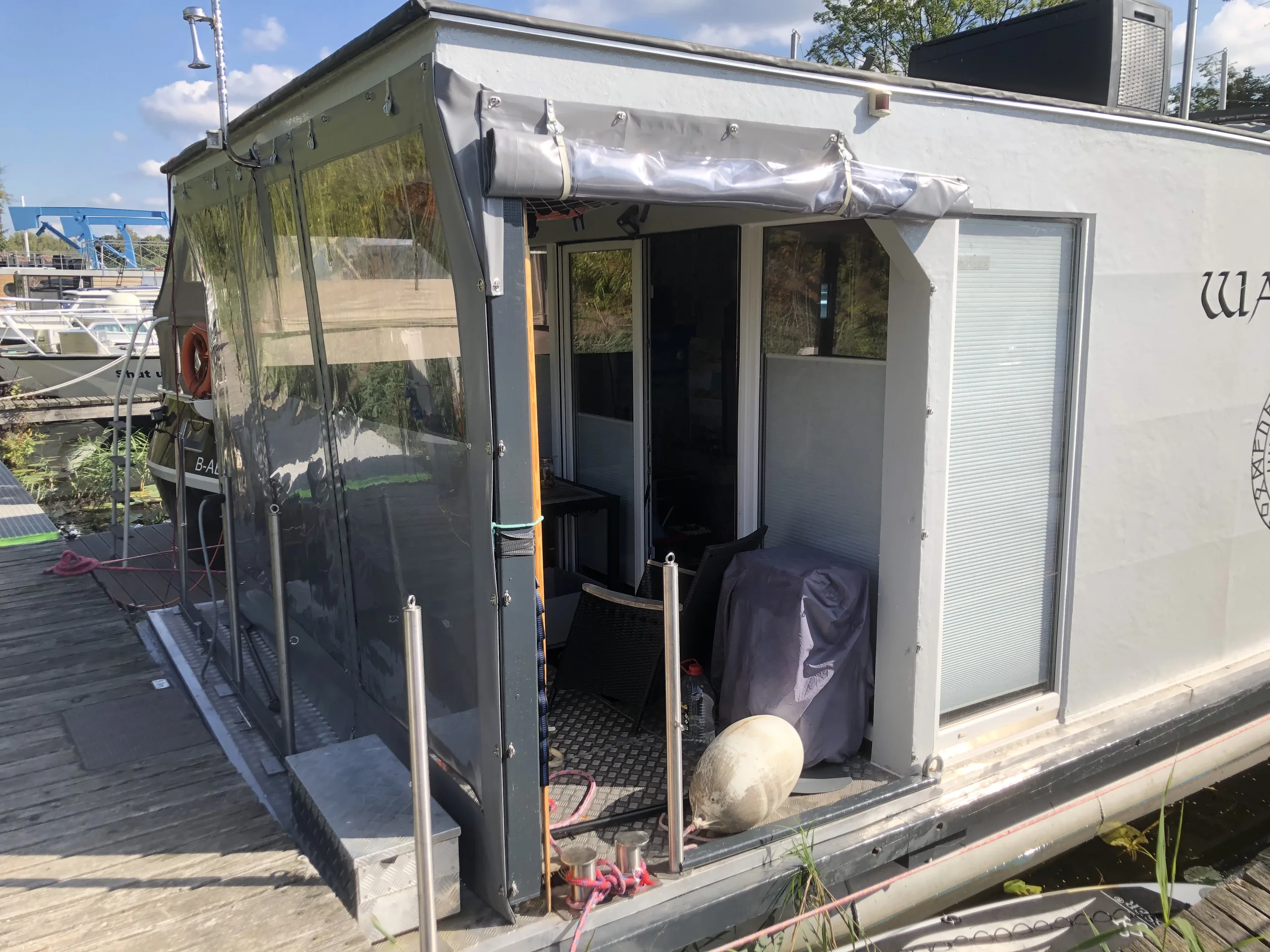 Transparente graue Einhausung mit geöffnetem Zugang an einem Hausboot.